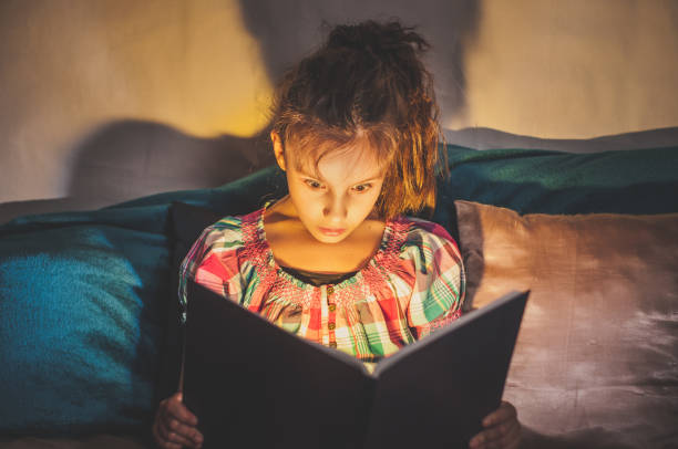 niña en la cama por la noche lee un terrible libro místico increíble en la oscuridad - child bedtime imagination dark fotografías e imágenes de stock