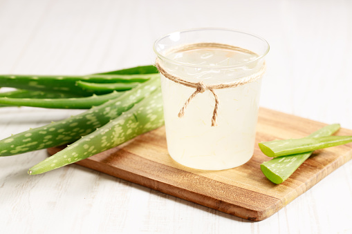 Healthy aloe vera juice in a glass with fresh aloe vara leaves on wooden paddle board