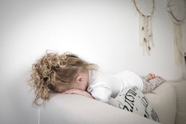 泣いている悲しい幼児の女の子はソファの上に横たわっている。子供の悲しみの概念。 - mad expression image front view horizontal ストックフォトと画像