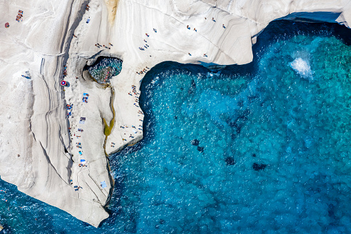 Aerial view to the chalk rock formations of Sarakiniko with people enjoying the sparkling blue sea on a hot summer day, Milos island, Cyclades, Greece