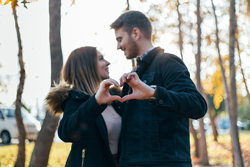 Shot of a a young couple making a heart shape with their fingers outdoors