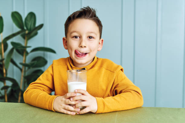 6-7 ans mignon enfant buvant du lait sur la table. il sait qu'il a besoin de boire du lait pour des os sains. il adore le lait. - 6 7 years photos et images de collection