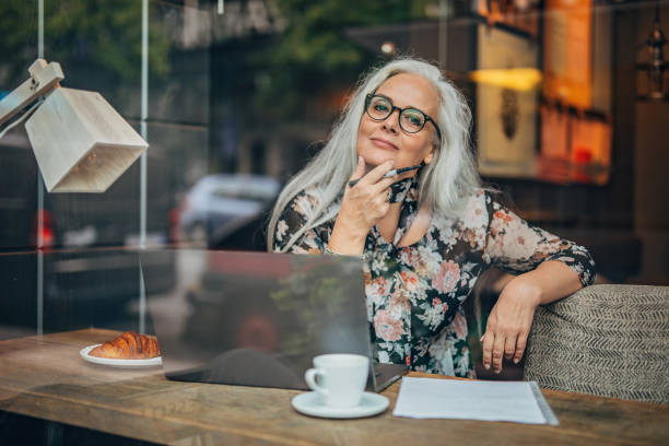 Old business woman sitting in cafe alone One woman, modern mature business lady sitting in cafe alone, using laptop. swedish woman stock pictures, royalty-free photos & images