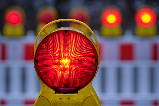 Closeup of a red warning light glowing in the dark at a construction site with street barriers in Germany in December