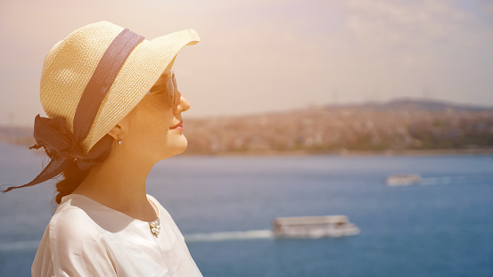 dreaming woman in sunhat stands half face enjoying vacation and looking into distance against blurry landscape closeup copyspace