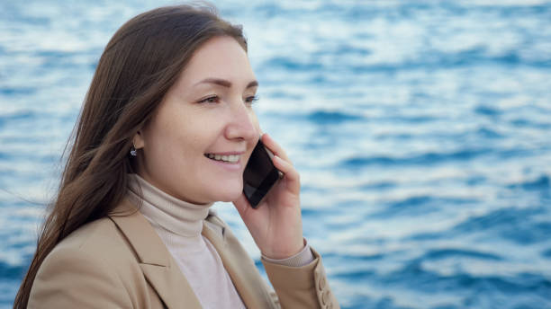 istock lady talks on phone standing on coast against blurry sea 1197622174