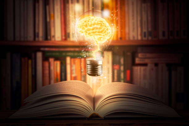 Glowing and shining brain lightbulb over an open book with a bookshelf as background. Knowledge, study, cognition, learning, literacy, library 3d illustration concepts. Mixed media. stock photo