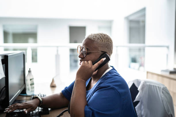 secretary talking on telephone at hospital reception - receptionist customer service customer service representative imagens e fotografias de stock