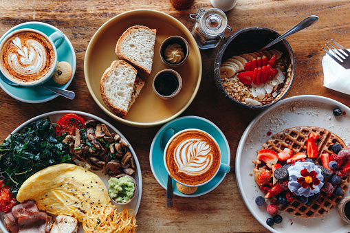 Morning breakfast on a table above, waffles with cream, berries, coffee, cappuccino, bowl, omlet with vegetables, bread with butter, avocado cream, vegan food, healthy food, meal