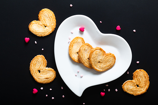 Valentine dessert food concept puff pastry hearts in white ceramic heart shape on black background with copy space