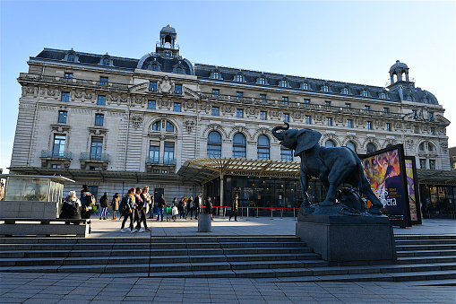 Paris, France- 12 18 2019:People walking in front of the facade of the Orsay museum in Paris.The Musée d'Orsay was originally a train station built for the 1900 World Exposition in Paris\nThe museum holds mainly French art,including paintings, sculptures, furniture, and photography.