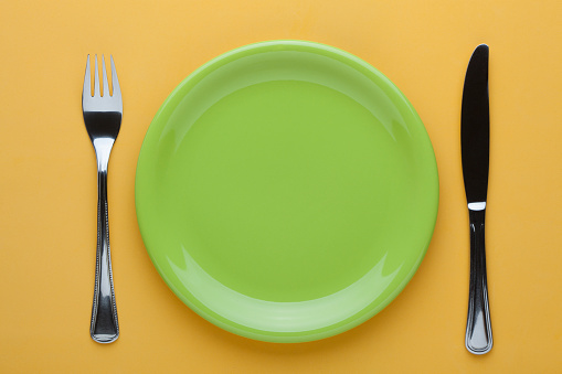 Empty plate with knife and fork on yellow background.