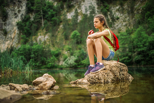 Girl sitting on the rock in the river, enjoying nature and eating apple. She is very cute and has healthy habits