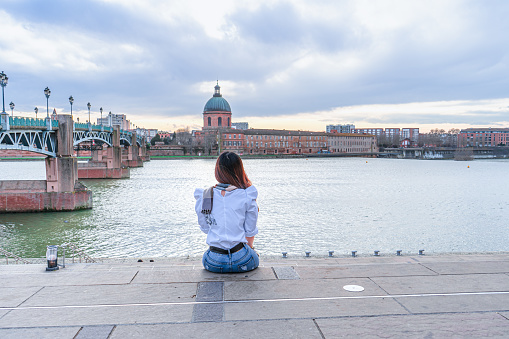 Asian woman sitting Garonne river and Dome de la Grave in Toulouse, France