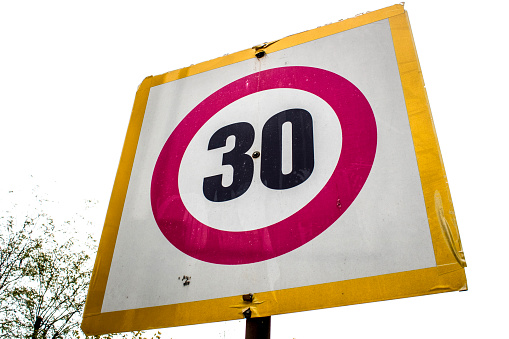 The speed limit is 30 km h. Photographed in cloudy weather. Writes 30 in black color on white surface in yellow frame.