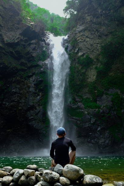 un giovane di fronte a una cascata con tonalità verde - ifugao foto e immagini stock