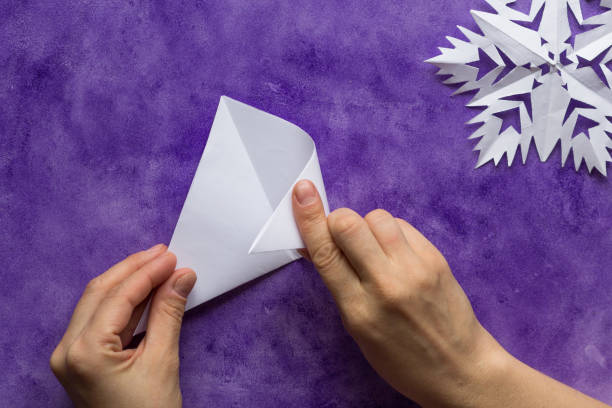Woman hands folding triangle sheet of paper in half to make smaller triangle on the violet surface Woman hands folding triangle sheet of paper in half to make smaller triangle on violet surface isosceles triangle stock pictures, royalty-free photos & images