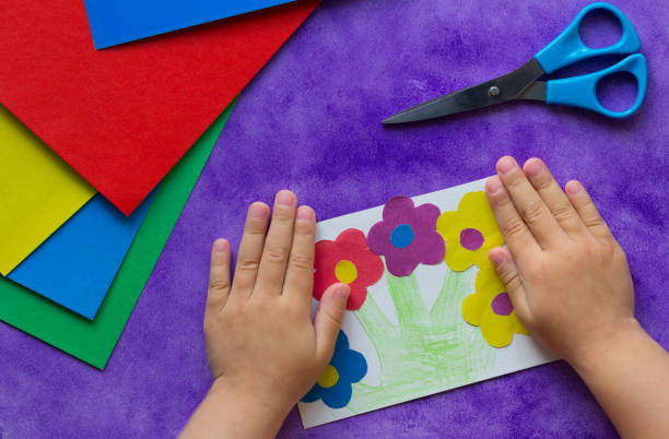 紫色の背景に子供の手に花を持つ手作りのグリーティングカード - fine motor skills ストックフォトと画像