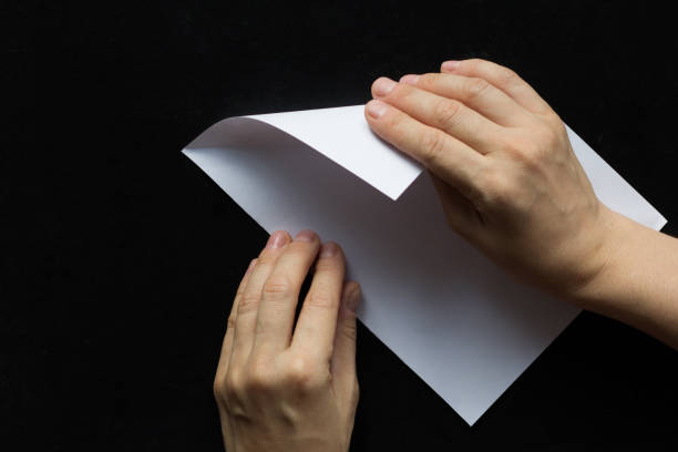 istock Woman hands folding rectangular sheet of paper to make it square on the black background 1197676914