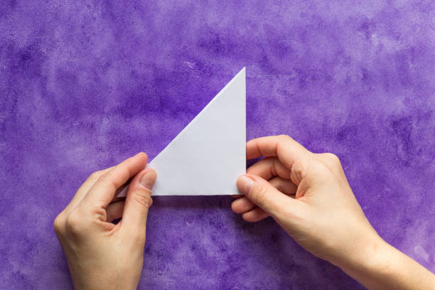 Woman hands holding made folded paper triangle on the violet surface Woman hands holding made folded paper triangle on violet surface isosceles triangle stock pictures, royalty-free photos & images