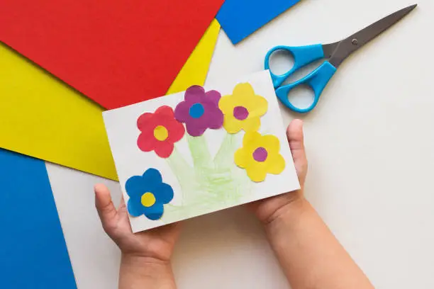 Handmade greeting card with flowers in child hands on the white background