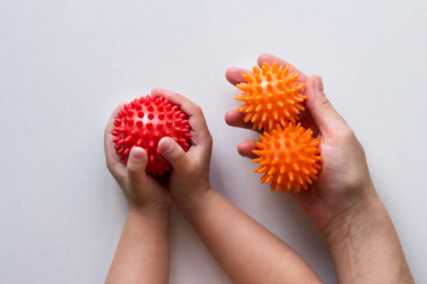 子供の手にスパイキーな赤いマッサージ針ボールと白い背景に女性の手で2つのオレンジ色のボール - fine motor skills ストックフォトと画像