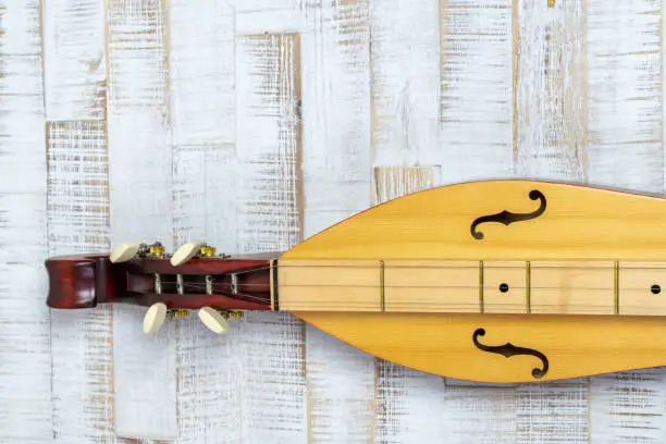 Detail view of an Appalachian mountain dulcimer musical instrument on a rustic white wooden background