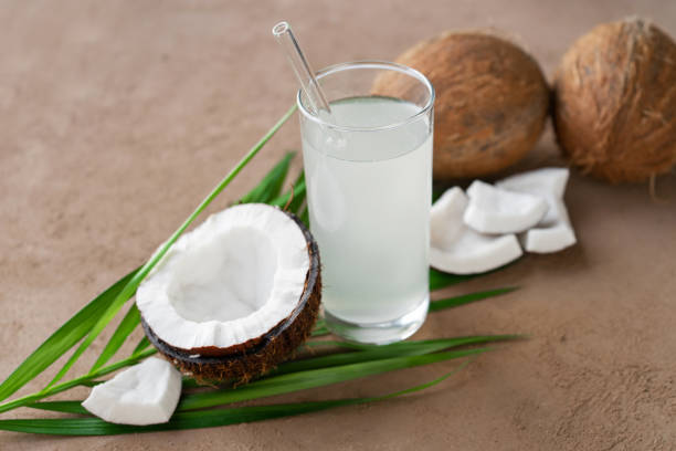 image of glass of coconut water, coconuts and palm leaf fresh coconuts and coconut water in glass with straw cocos stock pictures, royalty-free photos & images