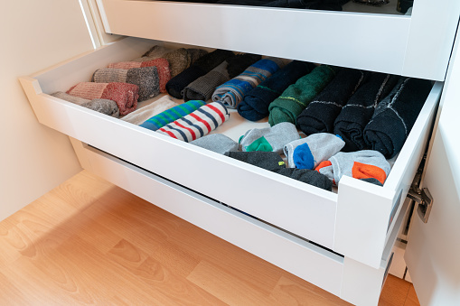 many colorful men's socks in a plain white wooden sock drawer in a large closet