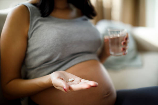 femme enceinte prenant la pillule à la maison - human pregnancy abdomen human skin healthcare and medicine photos et images de collection