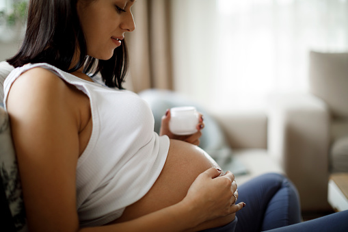 Mujer embarazada que aplica crema para el cuidado de la piel en su vientre para evitar la estría photo