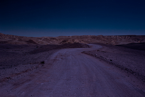 long exposure desert night scenery landscape with stars blue sky photography of wasteland country side gravel road go to mountains on horizon line background