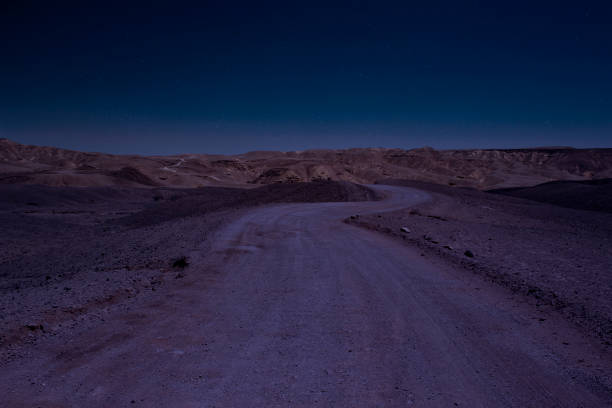 long exposure desert night scenery landscape with stars blue sky photography of wasteland country side gravel road go to mountains on horizon line background - desert road fotos imagens e fotografias de stock
