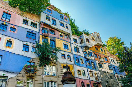 Vienna, Austria  - September 16, 2019:  Hundertwasserhaus apartment block has colorful facade, undulating floors, roof covered with earth and grass, large trees growing from inside the rooms