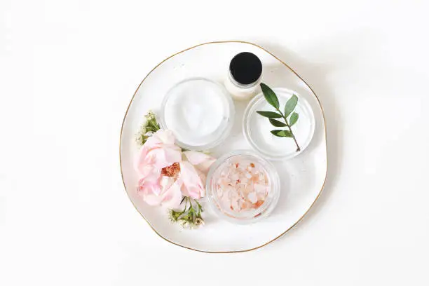 Styled beauty composition. Skin cream, shampoo bottle, rose flowers and Himalayan salt. White table background. Organic cosmetics, spa concept. Empty space, flat lay. Top view, web banner.