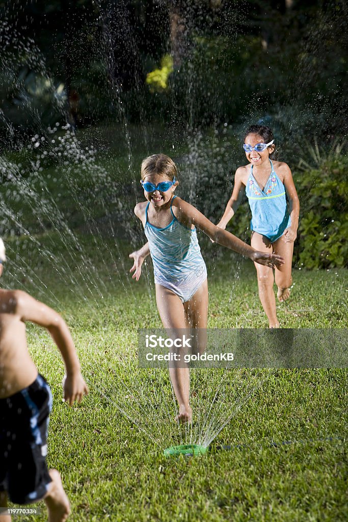 Children running through lawn sprinkler  Child Stock Photo