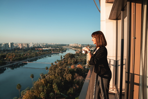 Young woman smiling and drinking some beverage and looking out from balcony.