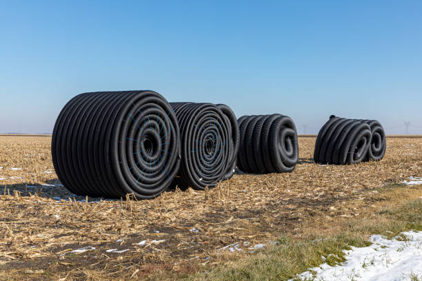 rolos enrolados da tubulação plástica plástica preta da drenagem, telha do campo, sentando-se no campo de exploração agrícola após a colheita pronta para ser enterrada no subsolo durante o inverno - controla da erosão - fotografias e filmes do acervo