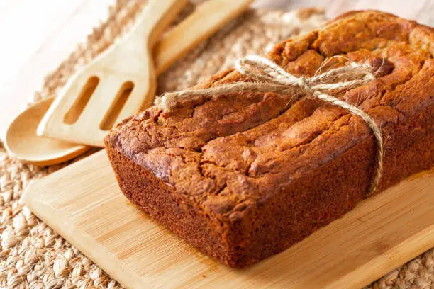 A loaf of banana bread made gluten free using almond flour with wooden utensils on cutting board