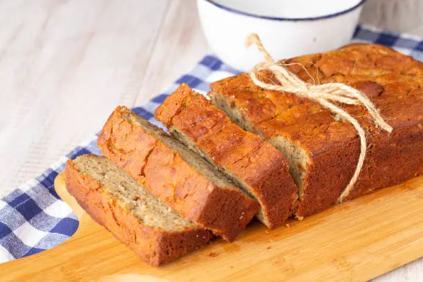 Banana bread with blue napkin and bowl on wooden cutting board