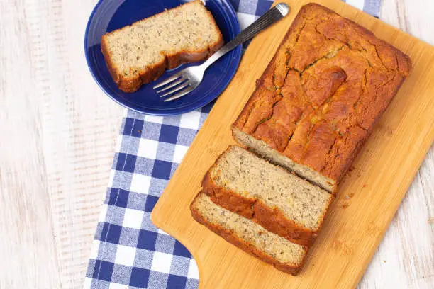 Banana bread made gluten free on wooden cutting board with slice on blue plate