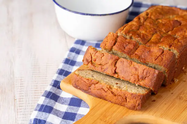 Breakfast treat of gluten free banana bread on wooden cutting board with blue napkin and bowl