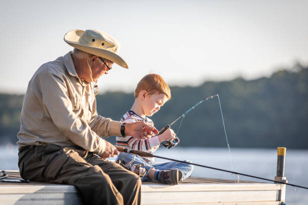 grand-père et petit-fils pêchant au coucher du soleil en été - fishing lake grandfather grandson photos et images de collection