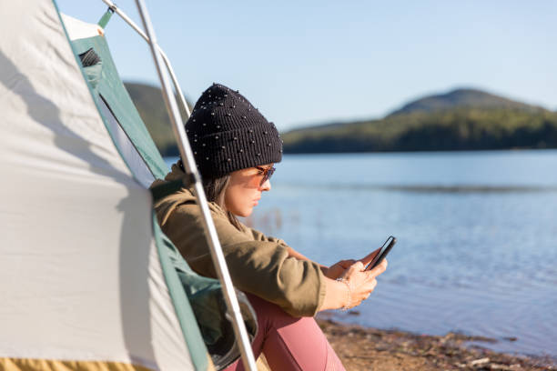 leitura das mulheres novas em seu telefone móvel pelo lago no acampamento - telephone nature mobile phone autumn - fotografias e filmes do acervo