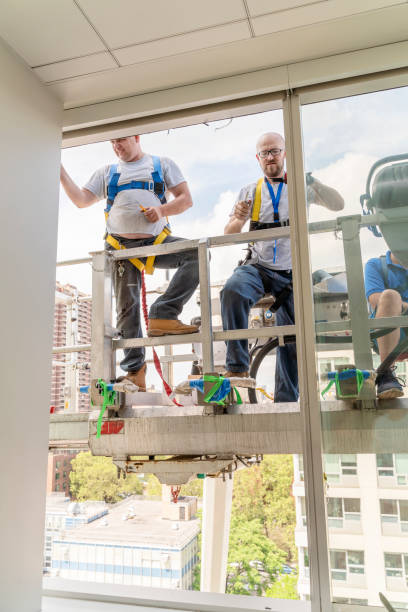 istock Team of blue-collar workers replacing a broken window in the office building - cleaning the frame after the old broken glass has been removed. High-altitude work on the lifting platform which is placed outside. 1197736100