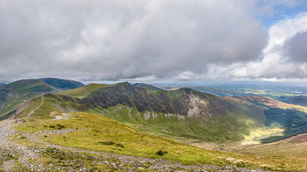 une vue scénique d'un sommet rocheux de montagne avec la pente verte herbeuse, le sentier et la chaîne de montagne à l'arrière-plan sous un ciel nuageux gris orageux - grass area hill sky mountain range photos et images de collection