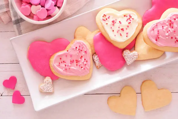 Photo of Heart shaped Valentines Day cookies with pink and white icing, overhead on a plate against white wood