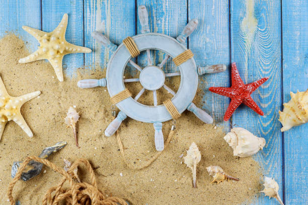 istock Decorative steering wheel with starfish, seashells on the sandy beach blue wood background 1197744401