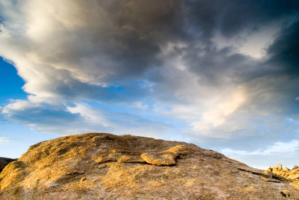 Round Crested surface of a sand colored high desert rock under a cloudy dynamic sky