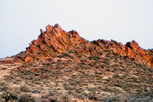 The dry rugged red colored rock boulders of the Owyhees in southwestern Idaho under the cloudy sky